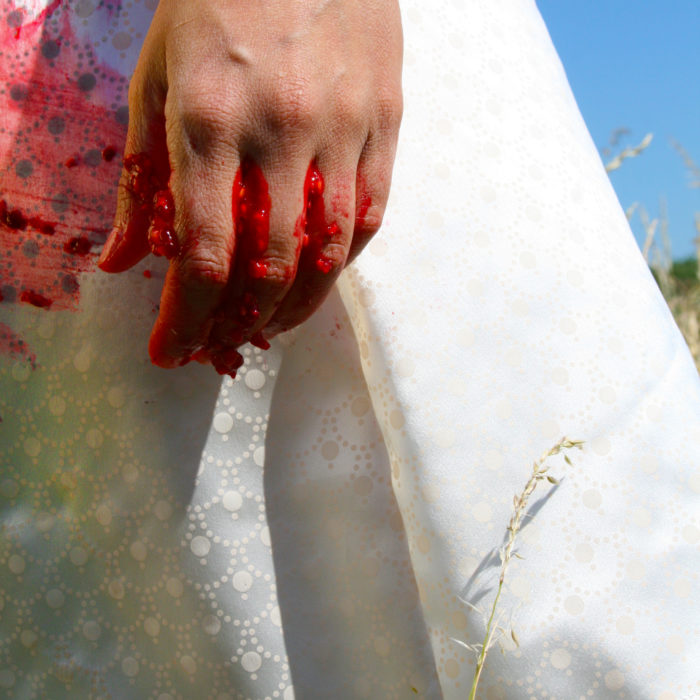 detail of white silk dress with hand and pink/blue details of fruit stains